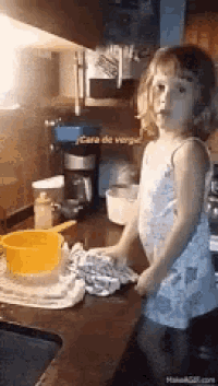 a little girl is standing in a kitchen with a yellow pot on the counter .