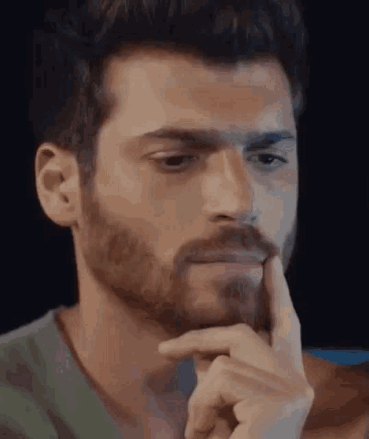 a man with a beard is holding his finger to his chin and looking at the camera .