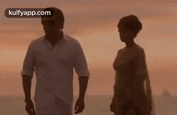 a man and a woman are standing next to each other on a beach at sunset .