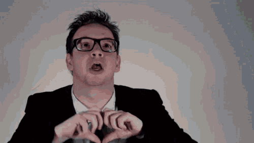 a man with glasses and a green tie making a heart shape with his hands