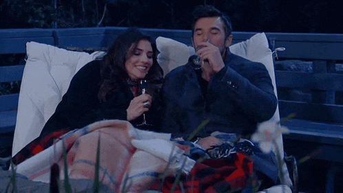 a man and a woman are laying on a bench drinking wine and smiling
