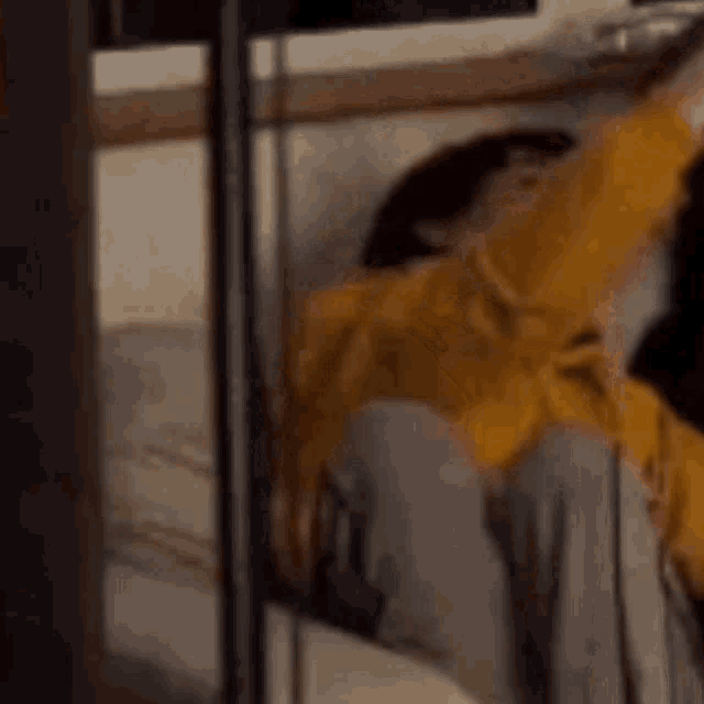 a man in a yellow jacket is sitting on a bed with his arm outstretched .