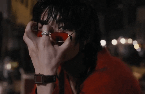 a woman wearing a red jacket and red sunglasses is covering her mouth with her hand .