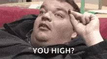 a fat man is laying on a bed with his hand on his forehead and saying `` you high '' .