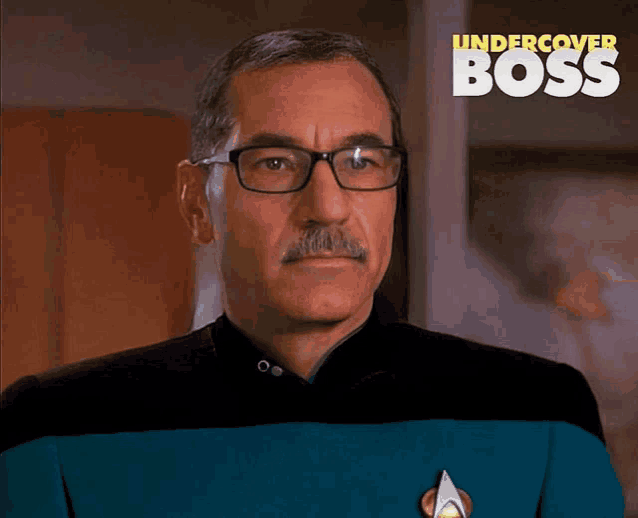a man with glasses and a mustache is standing in front of a poster that says undercover boss