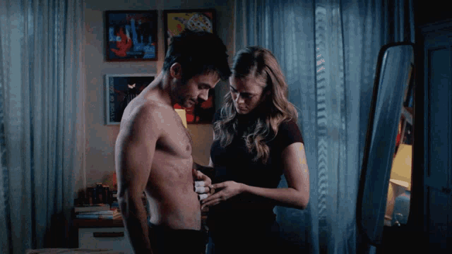 a man without a shirt is being examined by a woman in front of a mirror