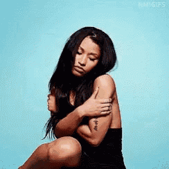 a woman in a black dress is kneeling down and hugging her arm .
