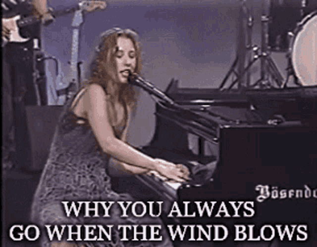 a woman singing into a microphone while playing a piano with the words why you always go when the wind blows below her
