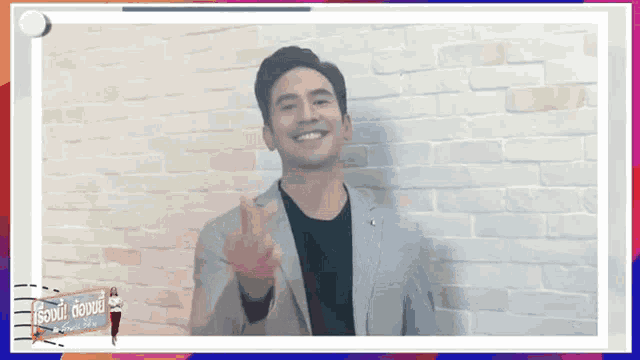 a man in a suit is smiling and giving a middle finger in front of a brick wall .