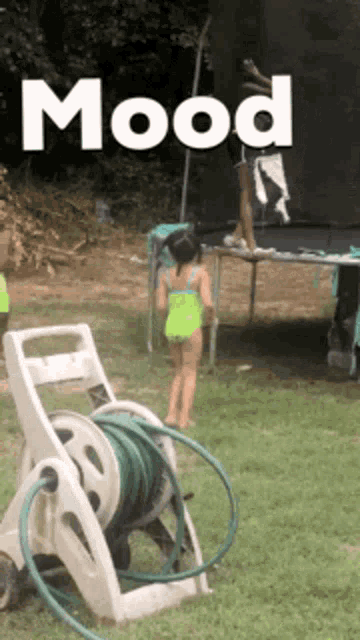 a girl in a green bathing suit is jumping on a trampoline while a hose reel is in the foreground