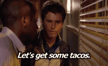 two men are standing next to each other in a hallway and they are talking about tacos .