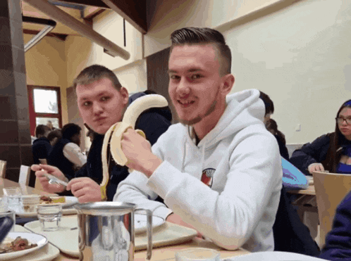 a man wearing a white tommy hilfiger sweatshirt eating a banana