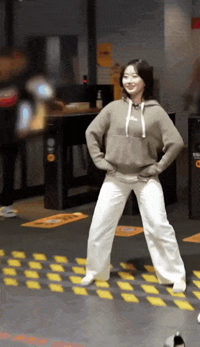 a woman in a brown hoodie and white pants is standing on a yellow and black striped floor .
