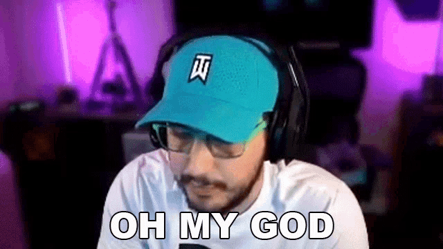 a man wearing a blue hat and headphones is sitting in front of a computer and says `` oh my god '' .