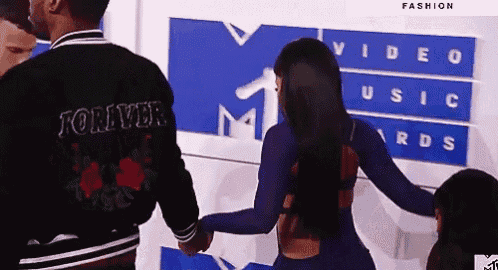 a man and a woman are holding hands in front of a sign that says video music awards
