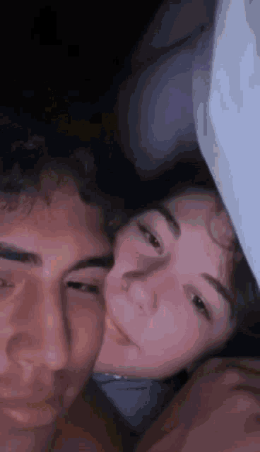 a man and a woman are laying under a blanket in bed .