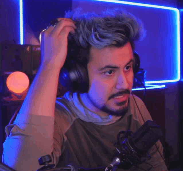 a man wearing headphones and a beard is sitting in front of a microphone in a room .