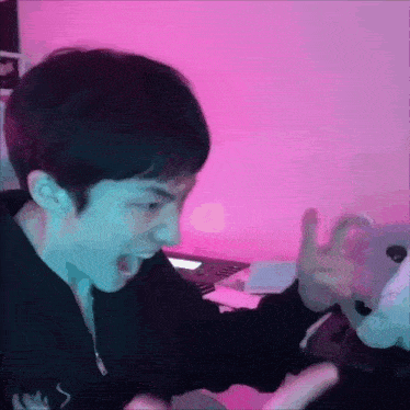 a young man is making a funny face while playing a video game in front of a pink wall .