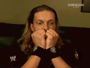 a man with long hair is sitting on a couch and covering his mouth with his hands while watching a sky sports live show