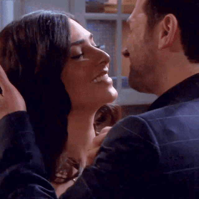 a man and a woman are kissing in a kitchen and the woman is smiling