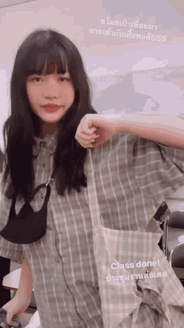 a girl wearing a plaid shirt and a black mask holds a tote bag in her hand ..