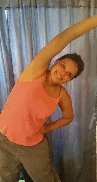 a woman in a pink tank top is stretching her arms in front of a window .