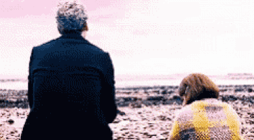 a man and a woman are sitting on a beach looking out at the ocean .
