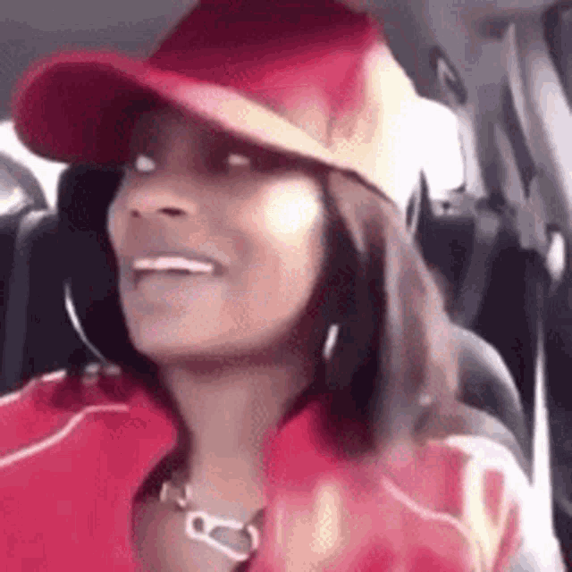 a woman wearing a red hat and a red jacket is sitting in a car and smiling .
