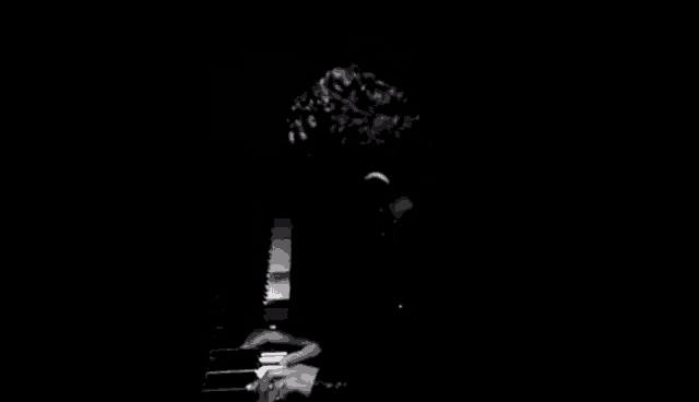 a black and white photo of a man playing a piano in the dark .