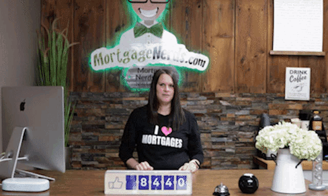 a woman wearing a shirt that says i love mortgages stands in front of a sign that says mortgage nerds.com