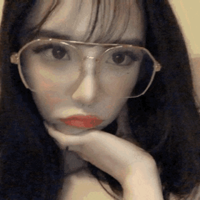 a woman wearing glasses and red lipstick holds her hand to her face