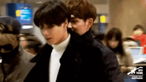 a man in a black jacket and a white turtleneck is walking through a crowd of people .