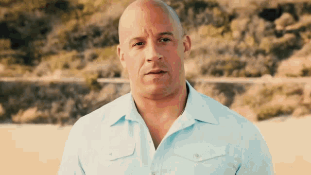 a bald man in a light blue shirt is standing on a beach .