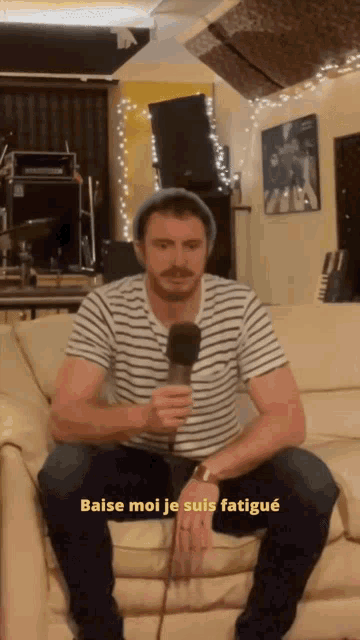 a man is sitting on a couch holding a microphone and says baise moi je suis fatigue