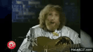 a man with a beard is singing into a microphone while holding a guitar .