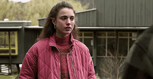 a woman wearing a pink jacket and a red sweater is standing in front of a building .
