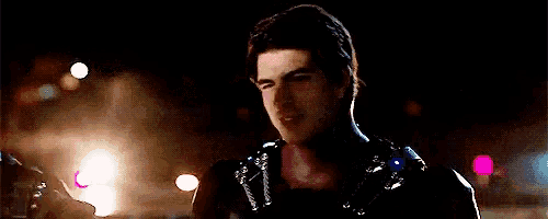 a man in a black leather jacket is standing in the dark looking at something .