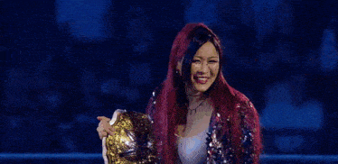 a woman with red hair is holding a wrestling championship belt and smiling .