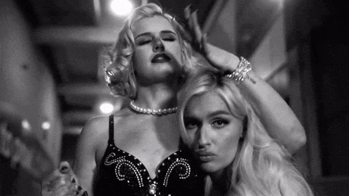 two women are posing for a black and white photo with one wearing a pearl necklace