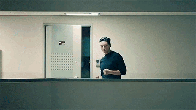 a man in a black sweater is standing in a hallway looking out a window .