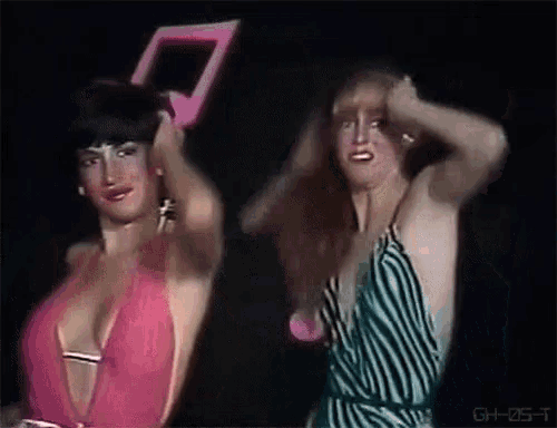 two women are dancing in front of a black background and one of them is wearing a pink top .