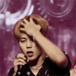 a man is singing into a microphone while holding his hand to his forehead .