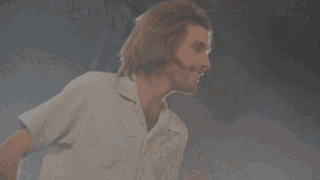 a man with long hair and a beard wearing a white shirt is smiling