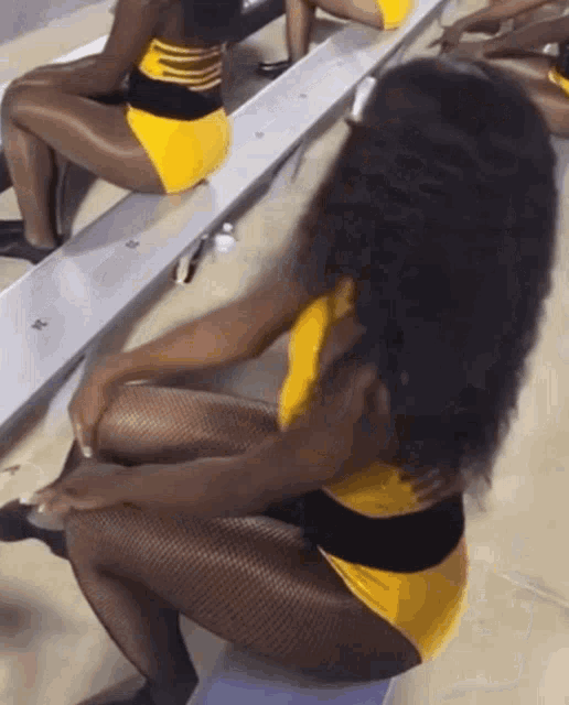 a group of cheerleaders are sitting on a bench with one wearing a yellow and black outfit