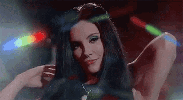 a woman with long black hair is standing in a dark room with a bunch of lights behind her .