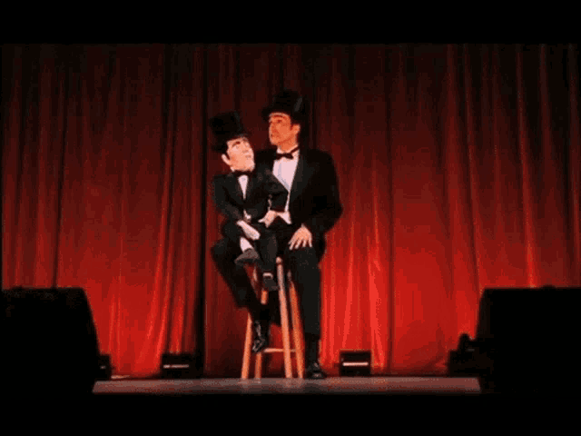 a man in a top hat stands next to a puppet in a tuxedo