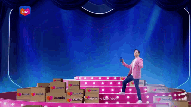 a man in a pink jacket is standing on a stage with boxes of lazada on it