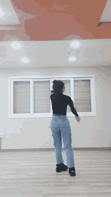 a woman in a black top and blue jeans is dancing in a room