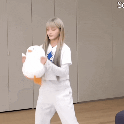 a woman in white pants is holding a stuffed duck in her hands
