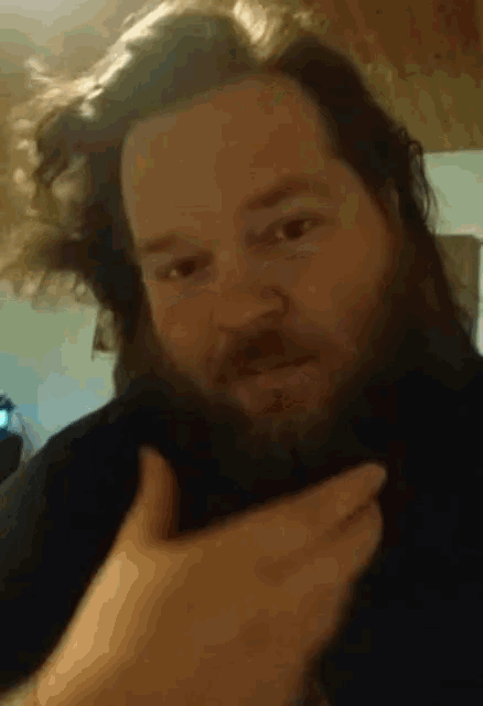 a man with long hair and a beard looks at the camera